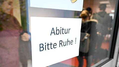 Abiturienten gehen kurz vor Beginn des Abiturs an einem Schild vorbei, auf dem "Abitur Bitte Ruhe!" steht. Foto: Felix Kästle/Archiv