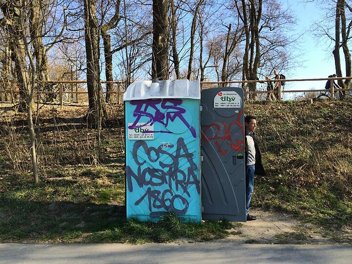 Neben der Wittelsbacher Brücke laufen Fußgänger, Jogger und fahren Radler. Unten verrichtet jemand seine Notdurft.
