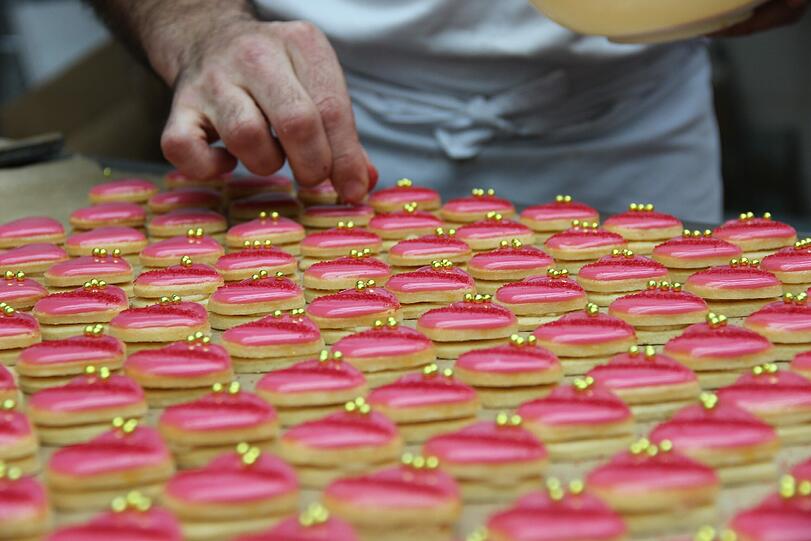 Die rosafarbenen Herzen werden von einem Mitarbeiter liebevoll mit goldenen Zuckerperlen verziert.
