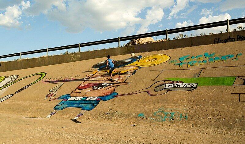 Die Kinder scheren sich nicht um diese etwas lächerlich wirkende Figur aus der Politik. Sie spielen auf der riesigen Graffiti-Karikatur an der Grenze zwischen Mexiko und den USA Fußball.