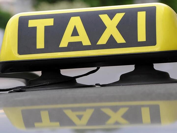 Ein Taxischild spiegelt sich auf einem Autodach. Foto: Franziska Kraufmann/dpa/Symbolbild