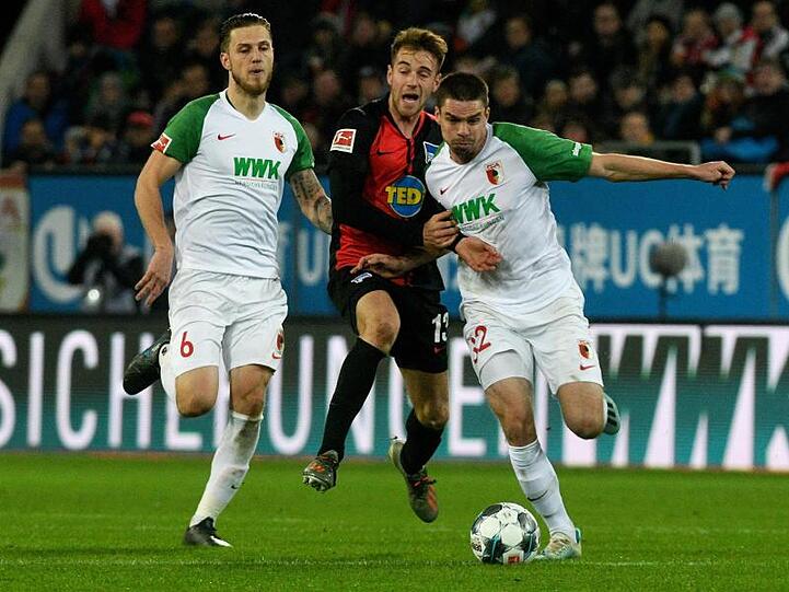 Raphael Framberger (r) und Jeffrey Gouweleeuw kämpfen mit Herthas Lukas Klünter um den Ball. Foto: Stefan Puchner/dpa/Archivbild
