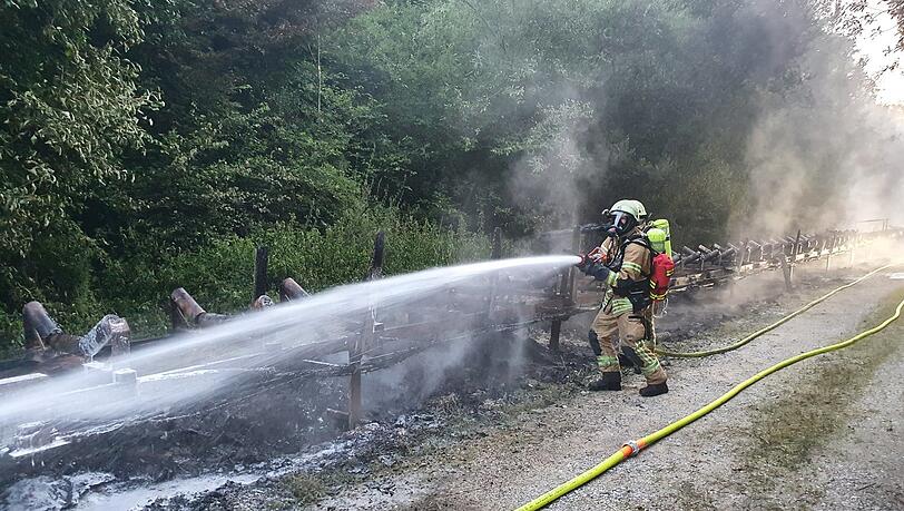 Feuerwehrleute löschen die letzten rauchenden Trümmer des ausgebrannten Förderbands.