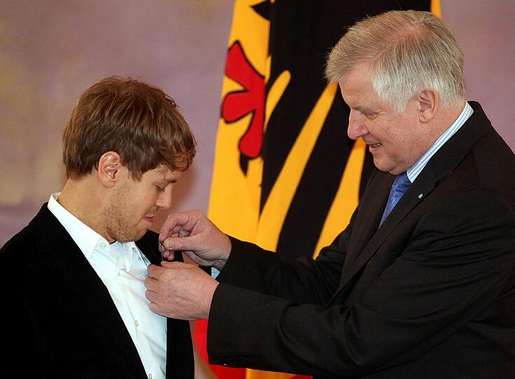 Mit kritischen Augen verfolgt Vettel, wie Seehofer ihm das Lorbeerblatt ans Revers ansteckt.