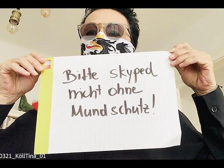 Ein Mann mit Mundschutz hält in einem Ausschnitt aus der "Corona-Rolle" ein Schild mit der Aufschrift "Bitte skyped nicht ohne Mundschutz" hoch.