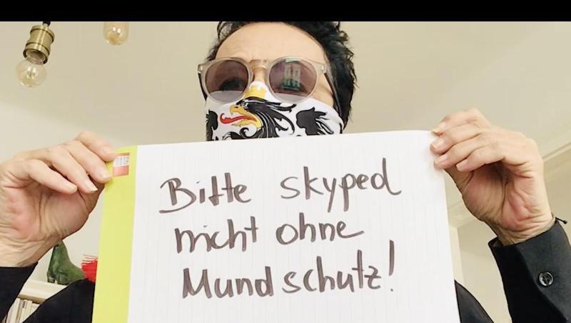 Ein Mann mit Mundschutz hält in einem Ausschnitt aus der "Corona-Rolle" ein Schild mit der Aufschrift "Bitte skyped nicht ohne Mundschutz" hoch. Ein Mann mit Mundschutz hält in einem Ausschnitt aus der "Corona-Rolle" ein Schild mit der Aufschrift "Bitte skyped nicht ohne Mundschutz" hoch.