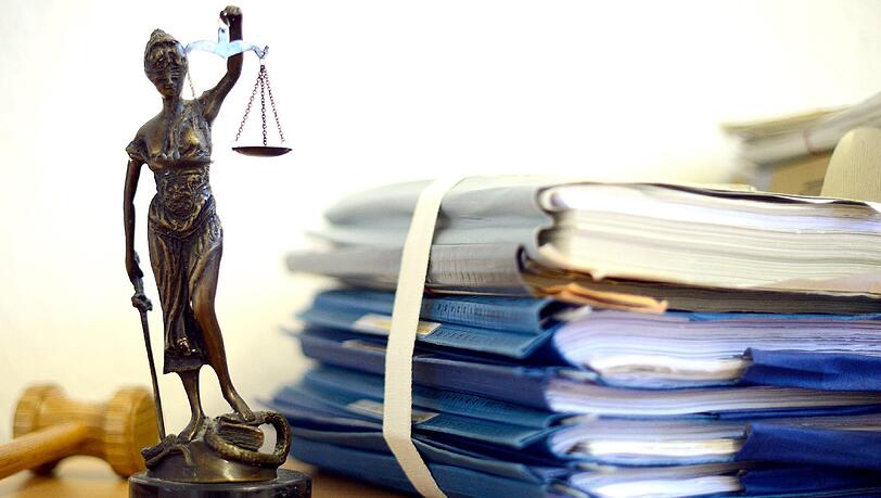 Eine Figur der Justitia, der altrömischen Göttin der Gerechtigkeit, neben einem Stapel Gerichtsakten. (Symbolbild) Eine Figur der Justitia, der altrömischen Göttin der Gerechtigkeit, neben einem Stapel Gerichtsakten. (Symbolbild)