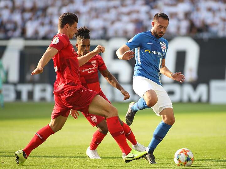 Rostocks Pascal Breier (r) wird von Daniel Didavi (M) und Mario Gomez unter Druck gesetzt.