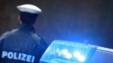 Ein Polizist steht im Regen vor einem Streifenwagen. Foto: Karl-Josef Hildenbrand/dpa/Archivbild