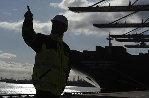 Ein Arbeiter steht vor einem Containerschiff im Hamburger Hafen. Foto: Marcus Brandt/Illustration