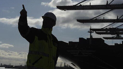 Ein Arbeiter steht vor einem Containerschiff im Hamburger Hafen. Foto: Marcus Brandt/Illustration Ein Arbeiter steht vor einem Containerschiff im Hamburger Hafen. Foto: Marcus Brandt/Illustration