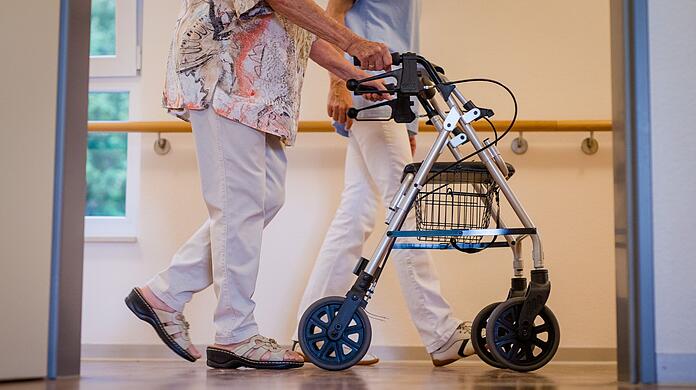 Eine Pflegekraft geht in einem Stuttgarter Pflegeheim mit einer älteren Frau über den Flur.
