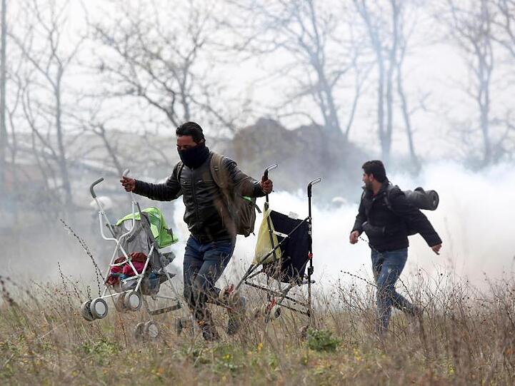 Ein Mann mit zwei Kinderwagen läuft vor Tränengas davon.