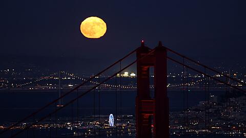 Hinter der Golden Gate Bridge ist am Himmel ein goldfarbener Vollmond zu sehen