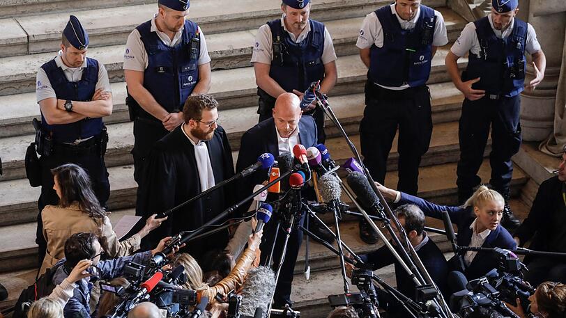 Die Rechtsanwälte Romain Delcoigne (Mitte, l) und Sven Mary (Mitte, r), Verteidiger des angeklagten IS-Terroristen Abdeslam, sprechen mit Journalisten im Brüssler Justizpalast nach dem Prozess gegen Abdeslam.