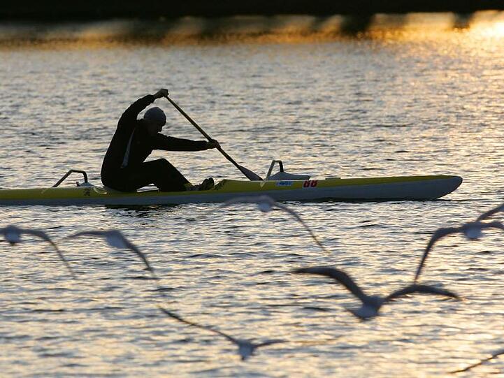 Ein Kanufahrer fährt bei Sonnenuntergang über das Wasser. Foto: Peter Steffen dpa/Archivbild