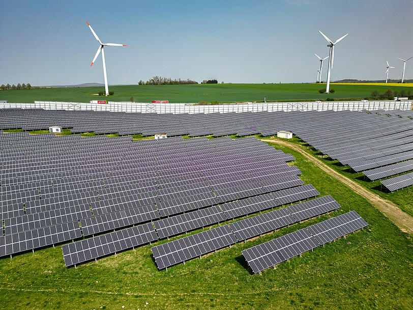 Mehrere Windkraftanlagen stehen hinter einem Solarpark. Energie aus Wind und Sonne ist effizienter als beispielsweise aus &Ouml;l.
