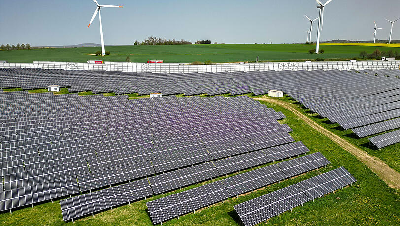 Mehrere Windkraftanlagen stehen hinter einem Solarpark. Energie aus Wind und Sonne ist effizienter als beispielsweise aus &Ouml;l.