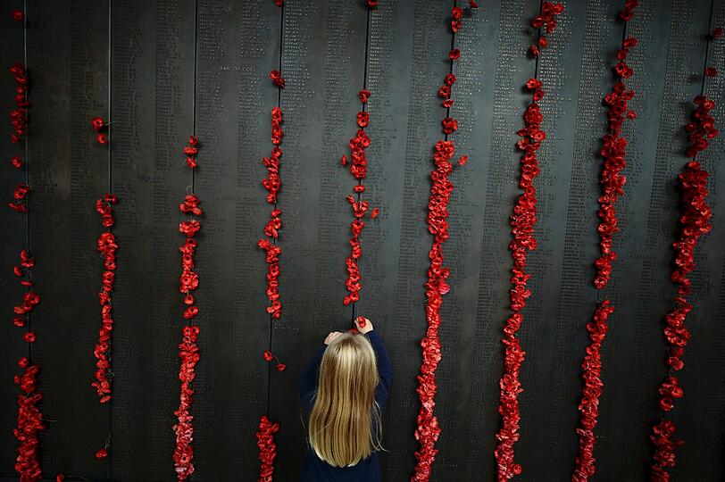 Ein kleines Mädchen klebt eine Mohnblume an die Gedenktafel eines Australischen Kriegerdenkmals in Canberra.