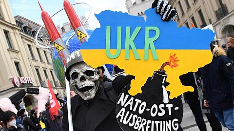 Ein Demonstrant mit Stahlhelm und Totenkopfmaske nimmt 2022 bei einer Demonstration gegen die Sicherheitskonferenz am Stachus teil.