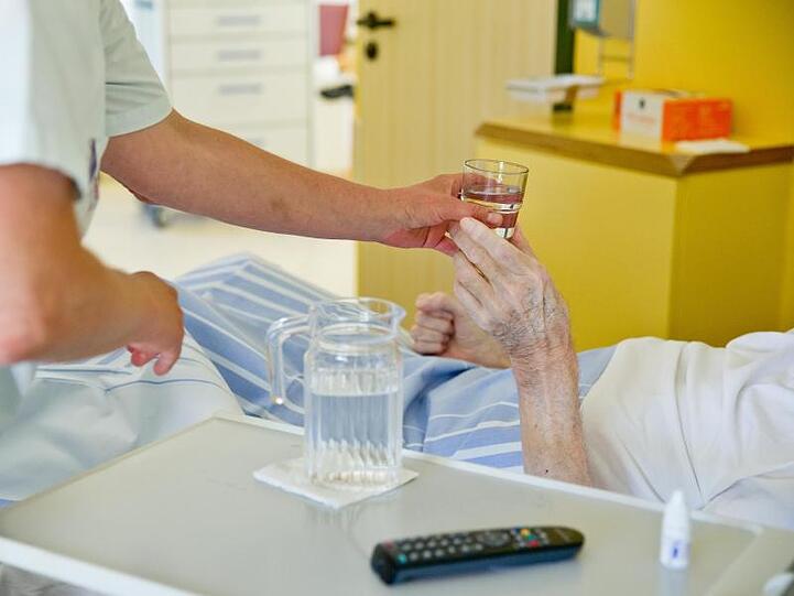 Eine Krankenpflegerin reicht einem Patienten in einem Klinikum ein Glas Wasser.