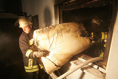Feuerwehrmänner schleppen Inventar aus der abgebrannten Wohnung. Nicht retten konnten sie die Hunde der Familie &ndash; die beiden Vierbeiner starben.