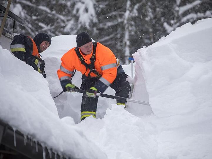 Feuerwehrmänner schaufeln in Buchenhöhe Schnee vom Dach eines Hauses.