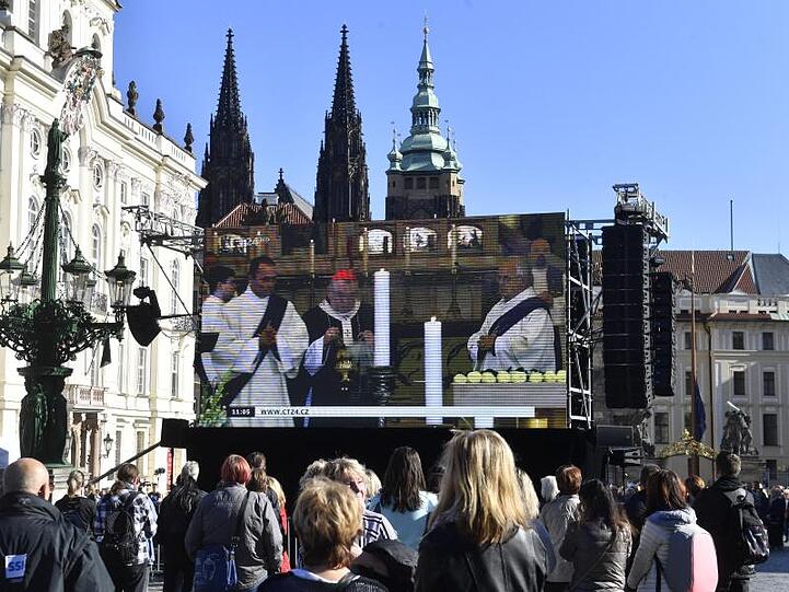 Fans stehen auf dem Hradschiner Platz und schauen auf einen Großbildschirm, auf dem die Trauerfeier für den Sänger Karel Gott im Prager Veitsdom übertragen wird. F.
