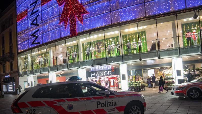 Polizeifahrzeuge stehen vor dem Kaufhaus Manor an der Piazza Dante im schweizerischen Kanton Tessin. Eine Frau hat in dem Warenhaus heute zwei Passantinnen mit einem Messer angegriffen.