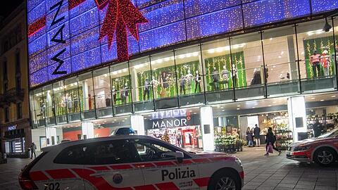 Polizeifahrzeuge stehen vor dem Kaufhaus Manor an der Piazza Dante im schweizerischen Kanton Tessin. Eine Frau hat in dem Warenhaus heute zwei Passantinnen mit einem Messer angegriffen.