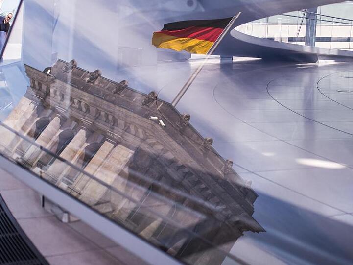 Eine Deutschland-Fahne spiegelt sich in der Kuppel des Reichstagsgebäudes.
