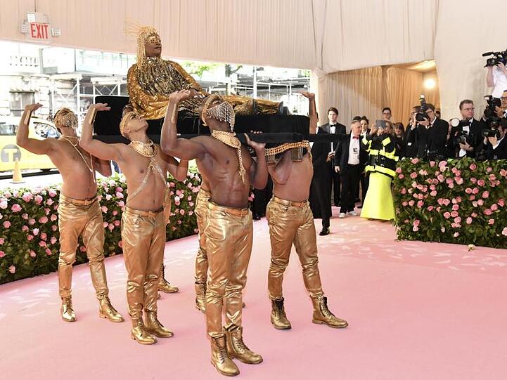 Der Entertainer Billy Porter schwebt auf einer Sänfte in den Saal, getragen von sechs gutgebauten Männern.