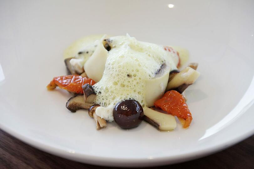 &bdquo;Trevisiano Crespelle&ldquo; mit Cardoncelli-Pilzen, Ofentomaten und Gorgonzola Dolce: Hinter dem Begriff verbirgt sich eine Safran-Nudelschnecke &ndash; die Pilzsorte Cardoncelli, besonders intensiv im Geschmack, hat Chefkoch Hausberger in Apulien entdeckt. Mit der Schmelzigkeit des Gorgonzola harmoniert der Graue Burgunder, der wie schon der Silvaner des ersten Ganges vom Gut Wernersbach stammt.