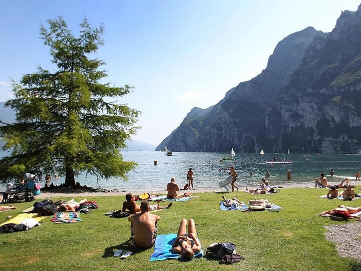 Touristen und Einheimische nehmen am Strand von Riva del Garda ein Sonnenbad.
