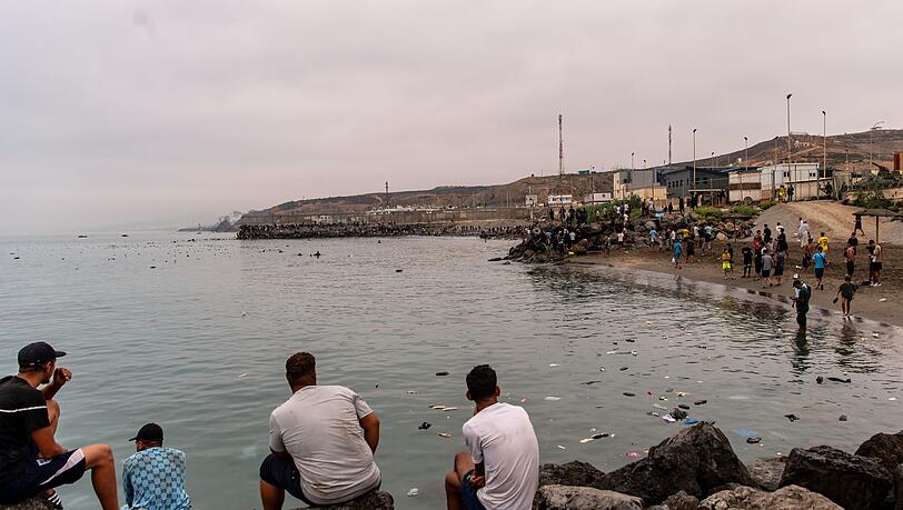 Migranten blickten von Felsen aus, während andere aus der spanischen Enklave Ceuta nach Marokko zurückkehrten. Migranten blickten von Felsen aus, während andere aus der spanischen Enklave Ceuta nach Marokko zurückkehrten.