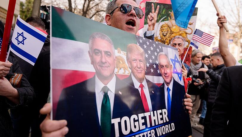 Ein Mitglied der iranischen Gemeinde h&auml;lt ein Plakat mit Abbildungen von von Irans exiliertem Kronprinzen Reza Pahlavi, US-Pr&auml;sident Donald Trump und Israels Ministerpr&auml;sident Benjamin Netanjahu w&auml;hrend einer Kundgebung vor der iranischen Botschaft in Bukarest.