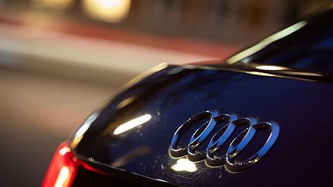 Das Logo vom Automobilhersteller Audi ist am Abend an einem Fahrzeug zu sehen.