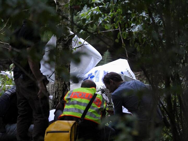 Einsatzkräfte der Polizei stehen am Wrack eines der abgestürzten Ultraleichtflugzeuge.