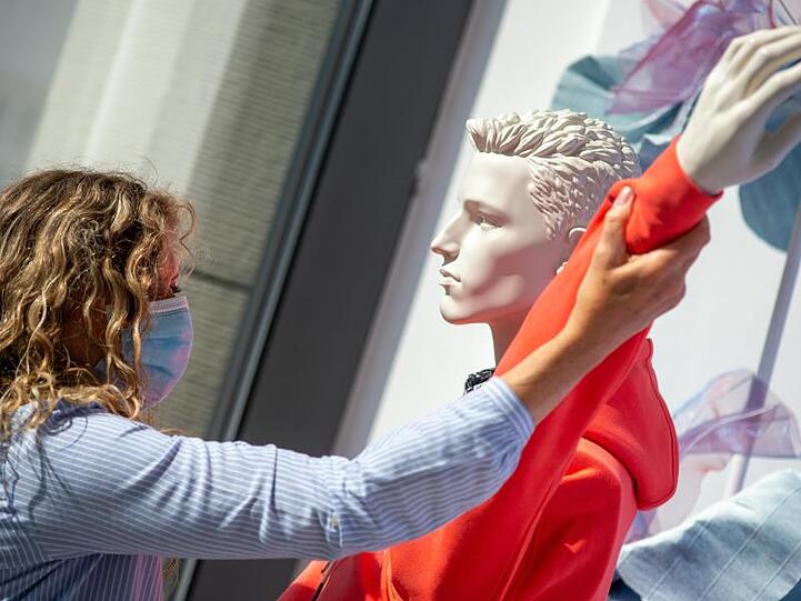 Eine Verkäuferin mit einem Mund-Nasen-Schutz entkleidet eine Puppe in einem Schaufenster. Foto: Klaus-Dietmar Gabbert/dpa-Zenralbild/dpa/Archivbild
