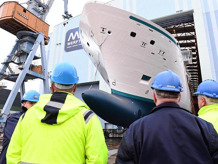 Mitarbeiter beobachten, wie ein Neubau auf der Stralsunder MV Werft eine Schiffbauhalle verlässt.