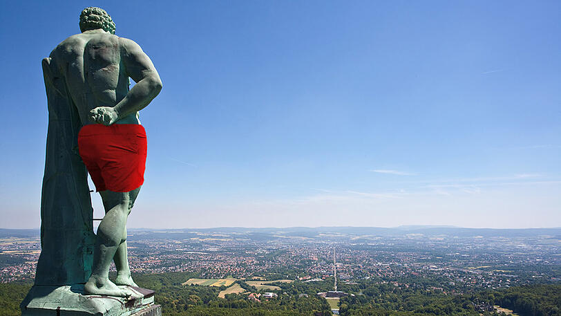 Die Kupferstatue des Herkules blickt bekleidet mit einer roten Badehose auf Kassel