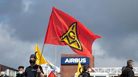 Beschäftigte eines Airbus-Werkes stehen vor den Toren des Werksgeländes und schwenken Fahnen der IG Metall.