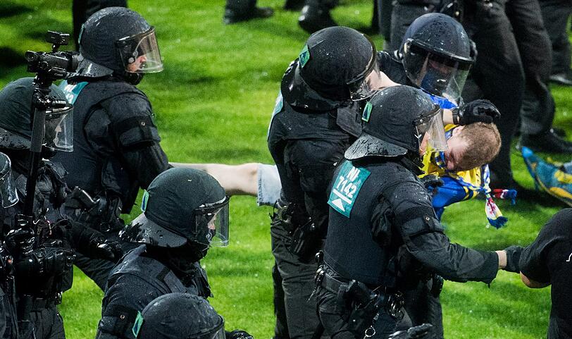 Braunschweiger Fans stehen Polizisten und Ordnern nach dem Abpfiff auf dem Platz gegenüber.