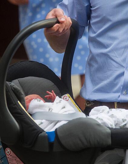 William trägt seinen Sohn in einem Babysitz zum Auto.