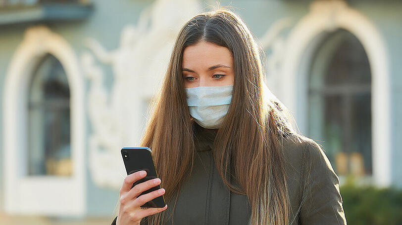 Eine junge Frau mit Schutzmaske und Smartphone. (Symbolbild)