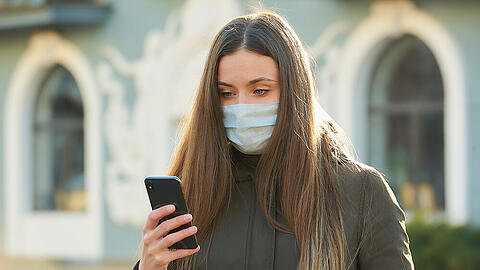 Eine junge Frau mit Schutzmaske und Smartphone. (Symbolbild)