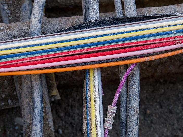 Bunte Glasfaserkabel für die Telekommunikation liegen in einer Baugrube zwischen anderen Leitungen. Foto: Peter Kneffel/Archivbild