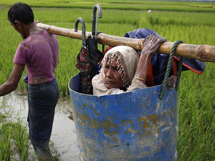 Flüchtlinge der Rohingya tragen eine alte Frau über einen schlammigen Weg, nachdem sie die Grenze zwischen Bangladesch und Myanmar überquert haben.