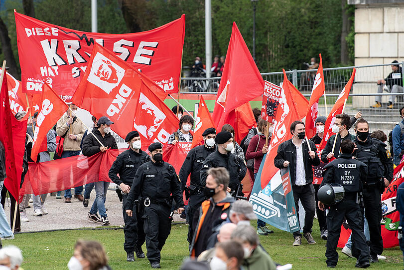 Polizisten begleiten die DGB-Kundgebung auf dem Königsplatz. Um sie herum stehen zahlreiche Demonstrationsteilnehmer mit Banner der Deutschen Kommunistischen Partei (DKP).