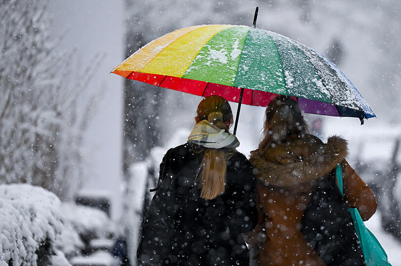 Zwei Frauen stapfen mit einem buntem Regenschirm durch den Schnee.